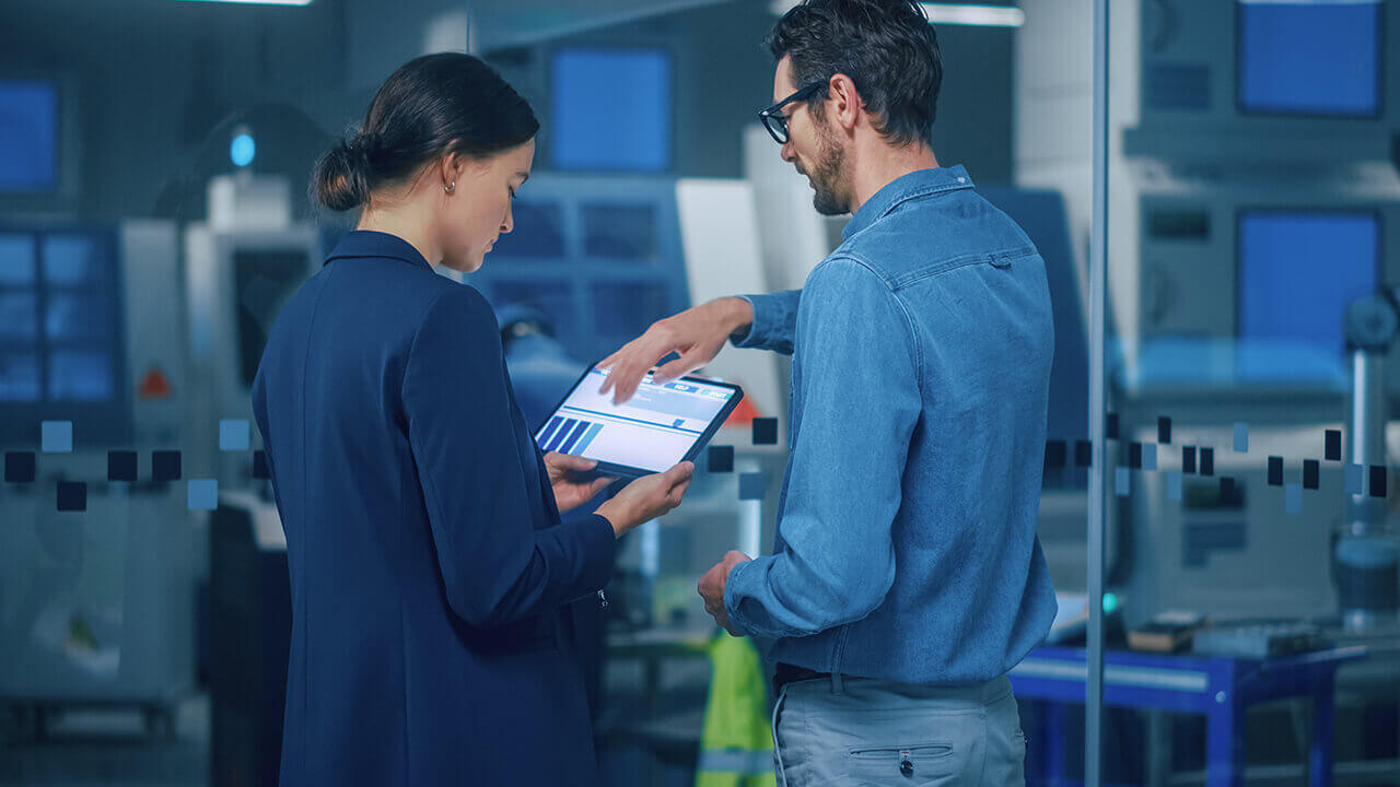 Female project manager and male engineer discussing in a factory, using tablet computer.